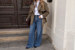 Look autunnale da donna con jeans wide leg blu, camicia bianca e giacca corta marrone, per un outfit casual chic dallo stile urbano e contemporaneo.